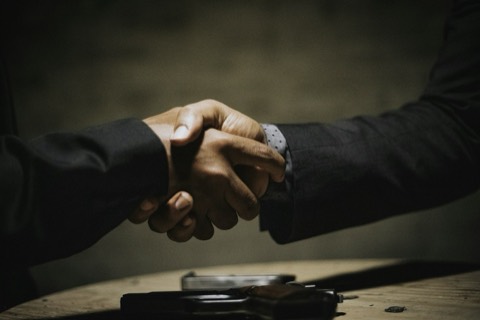 Dos personas estrechándose la mano sobre una mesa al cerrar un trato
