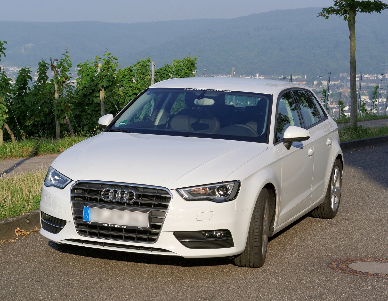 Audi A3 Sportback 8V blanco de tres cuartos delantero en una carretera secundaria entre viñedos
