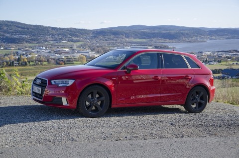 Audi A3 Sportback 8V rojo de tres cuartos delantero, aparcado sobre grava con un fiordo y colinas al fondo