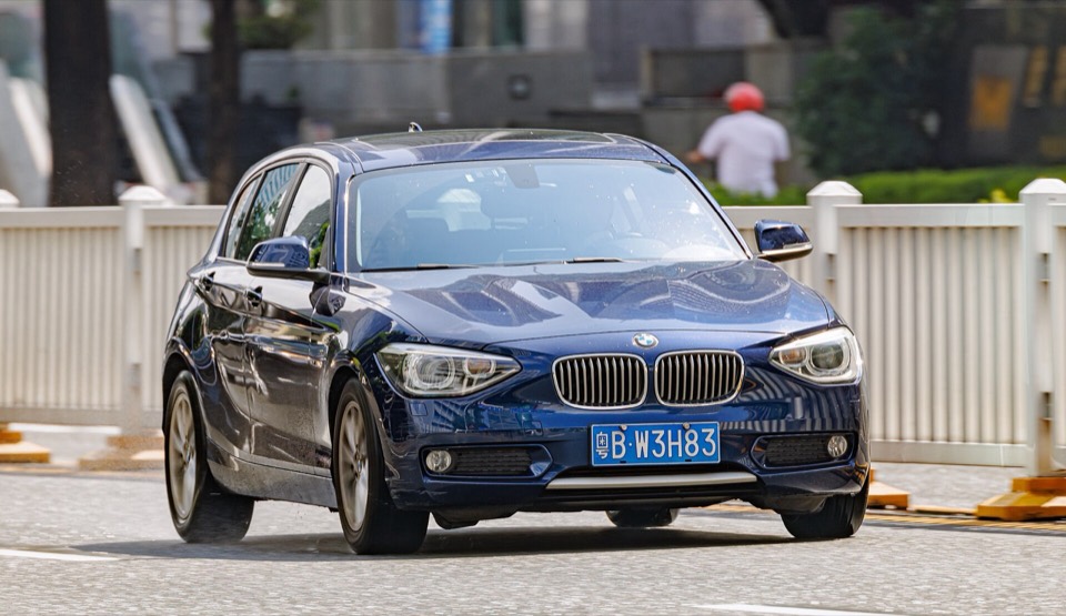 BMW Serie 1 F20 azul oscuro visto de frente circulando por una avenida