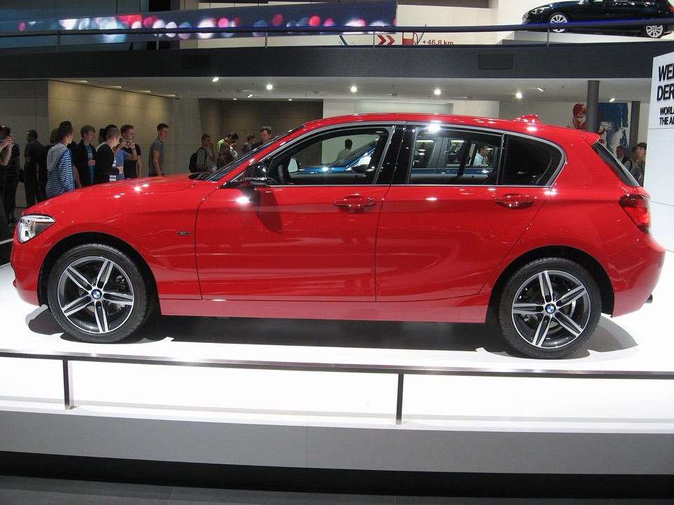 BMW Serie 1 F20 rojo de perfil, con las llantas y la proporción del capó largo a la vista