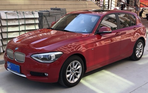 BMW Serie 1 F20 rojo de tres cuartos delantero aparcado en la calle con luz de mediodía