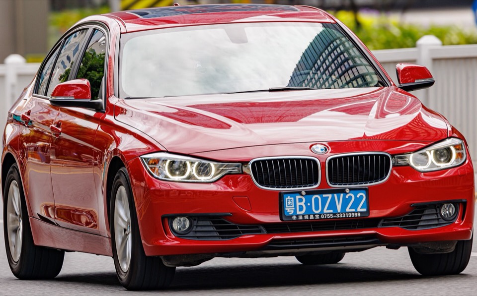 BMW Serie 3 F30 rojo de tres cuartos delantero circulando por una calle con luz natural