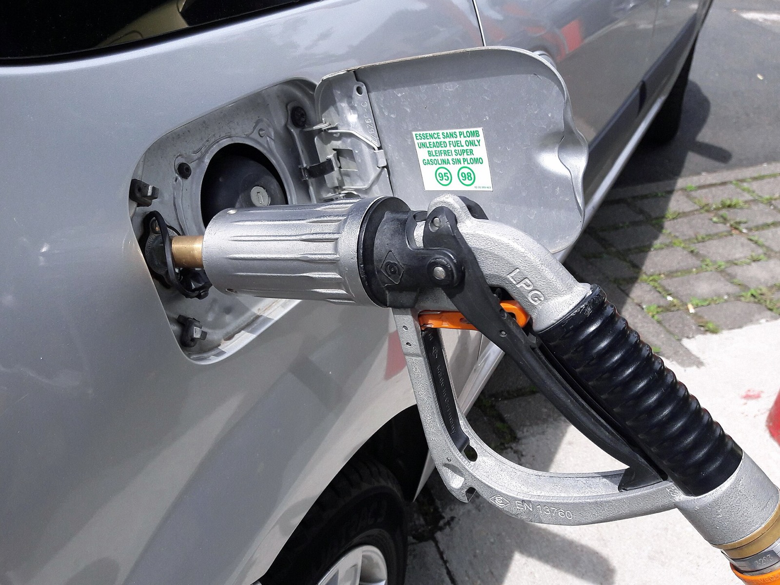 Boquerel de autogás GLP acoplado a la boca de llenado de un coche, junto a la pegatina de gasolina sin plomo