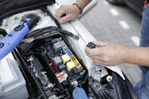 Manos revisando la caja de fusibles de un coche