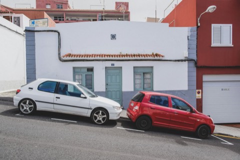 Dos coches aparcados en una calle española, frente a una fachada blanca con puerta de garaje