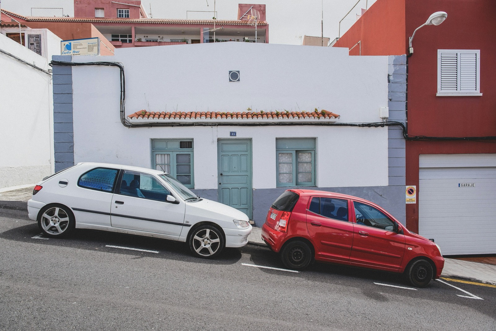 Dos coches aparcados en una calle española, frente a una fachada blanca con puerta de garaje