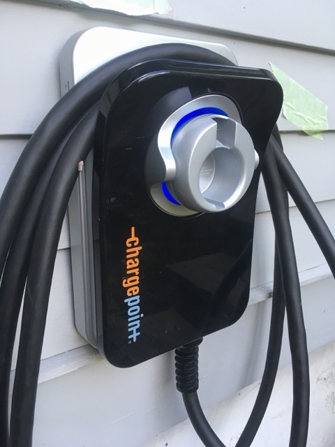 Cargador de coche eléctrico montado en la pared exterior de una vivienda, con el cable recogido