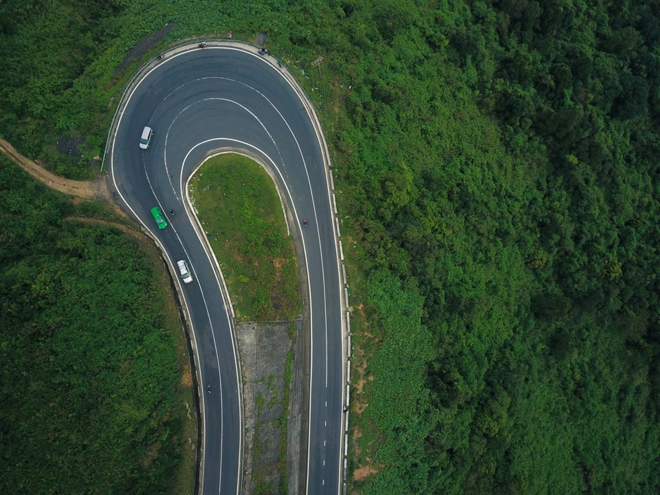 Vista aérea de una carretera de montaña en herradura entre vegetación, con varios coches circulando