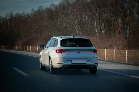 Coche blanco circulando por una carretera comarcal junto a un bosque