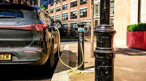 Coche eléctrico enchufado a un poste de recarga en la calle de una ciudad