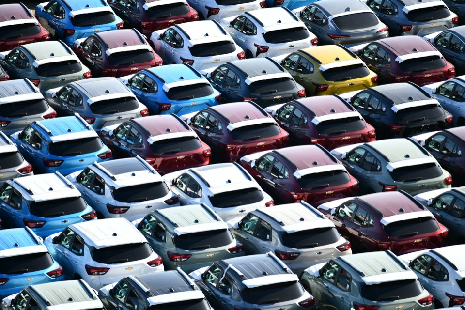 Filas de coches nuevos de distintos colores aparcados en una campa, vistos desde arriba