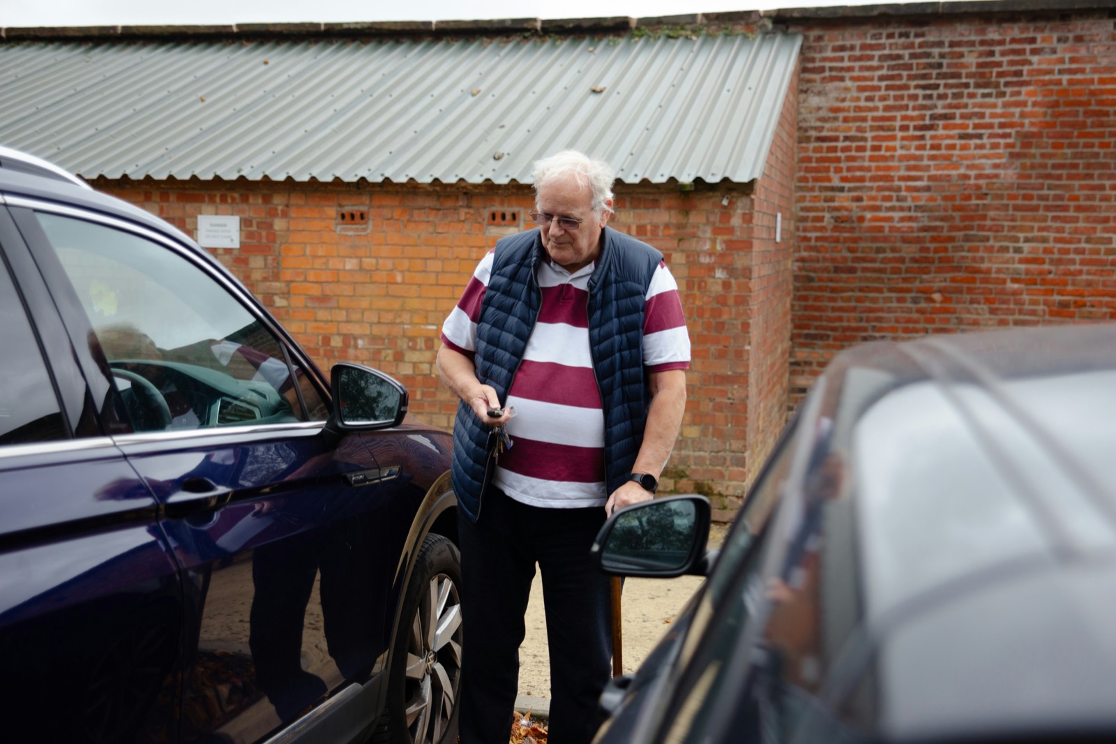Persona mayor de pie junto a un coche en la calle