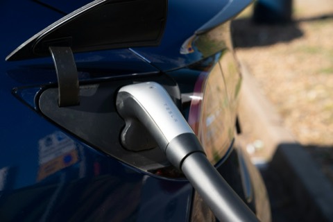 Conector de carga enchufado en la toma de un coche eléctrico azul oscuro