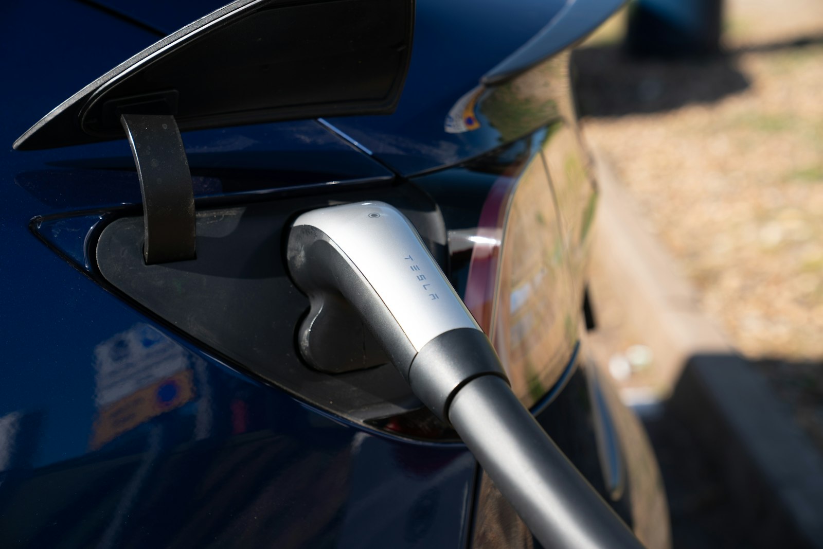 Conector de carga enchufado en la toma de un coche eléctrico azul oscuro