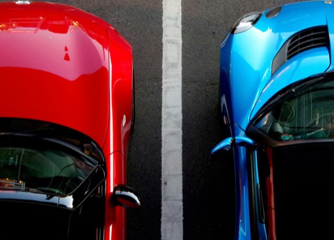 Vista cenital de dos coches, uno rojo y otro azul, aparcados a ambos lados de una línea blanca