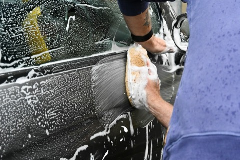 Persona lavando un coche a mano con una esponja