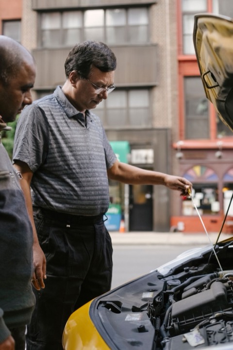 Persona inspeccionando el vano motor de un coche con el capó abierto
