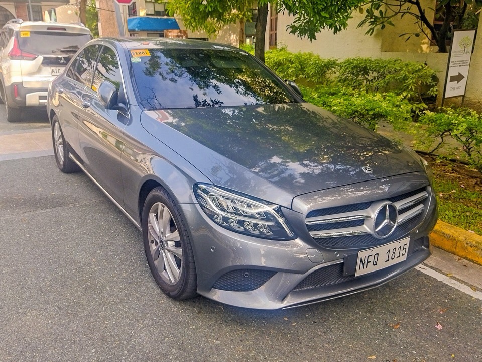 Mercedes Clase C W205 gris aparcado en una calle urbana con vegetación al fondo