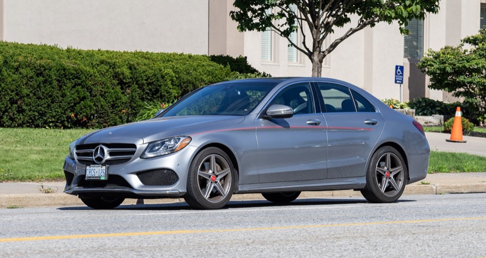 Mercedes Clase C W205 gris de tres cuartos delantero aparcado en una calle arbolada con luz de día