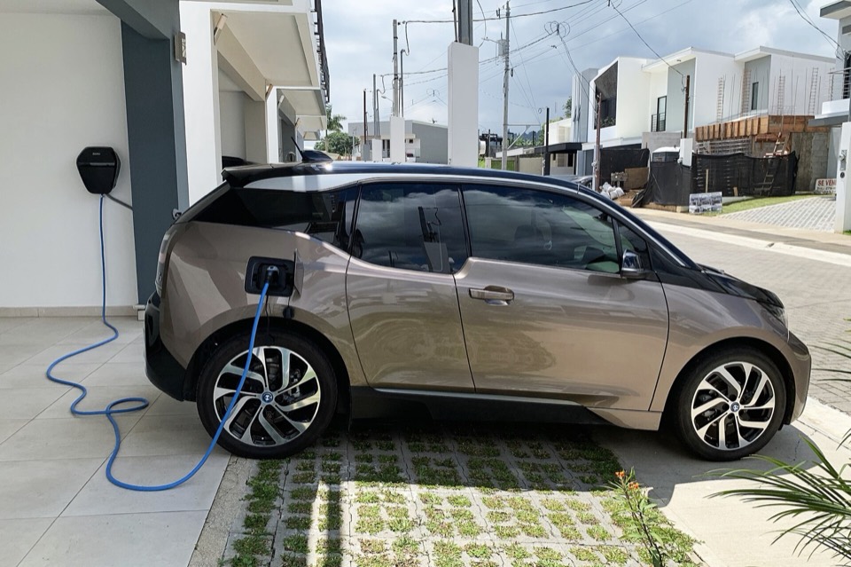 Coche eléctrico enchufado a un punto de recarga doméstico en el acceso de una vivienda