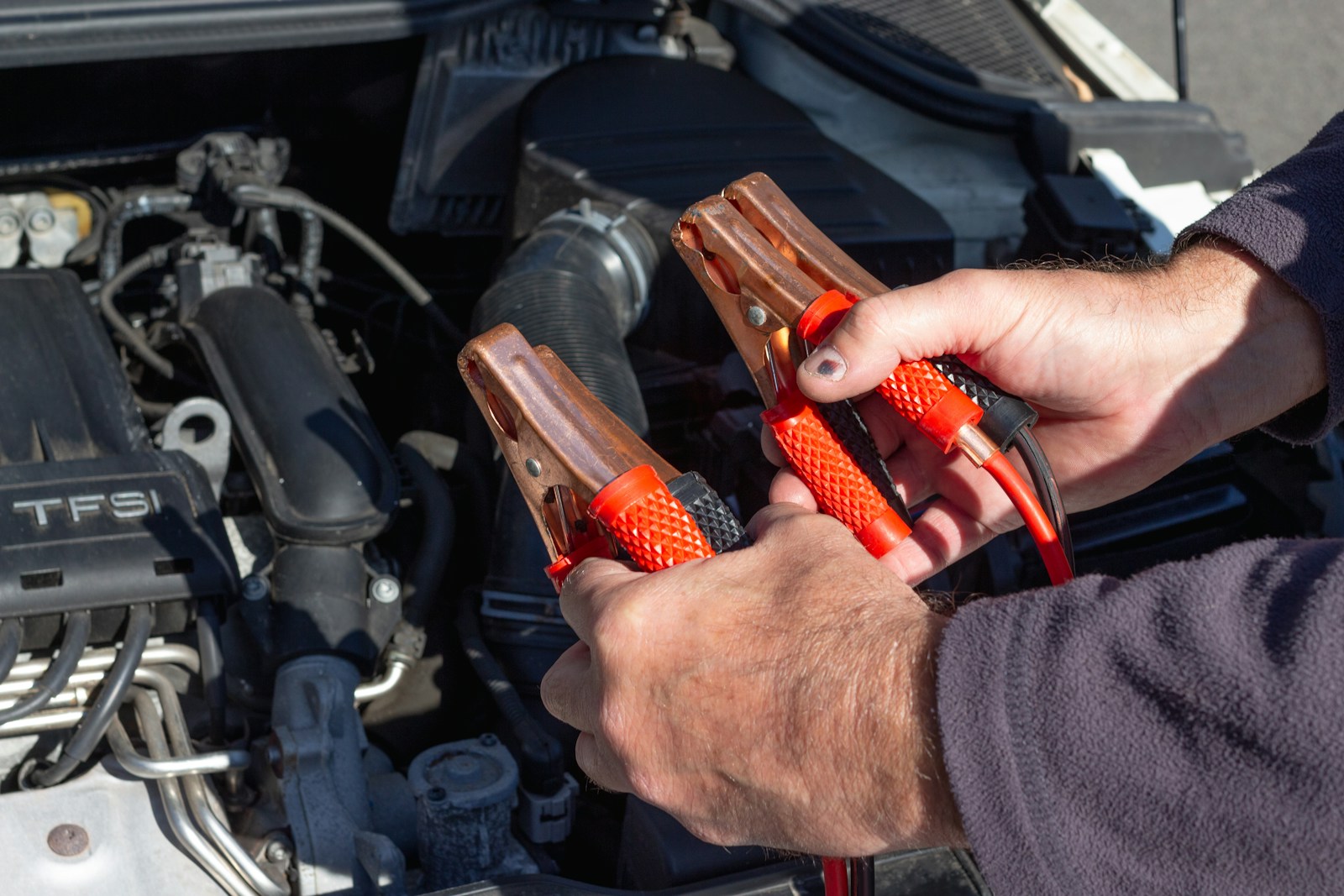 Manos conectando unas pinzas de arranque rojas y negras en el vano motor de un coche