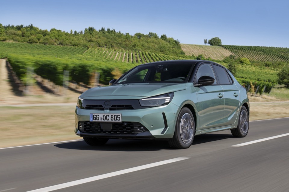 Opel Corsa verde claro circulando por una carretera entre viñedos