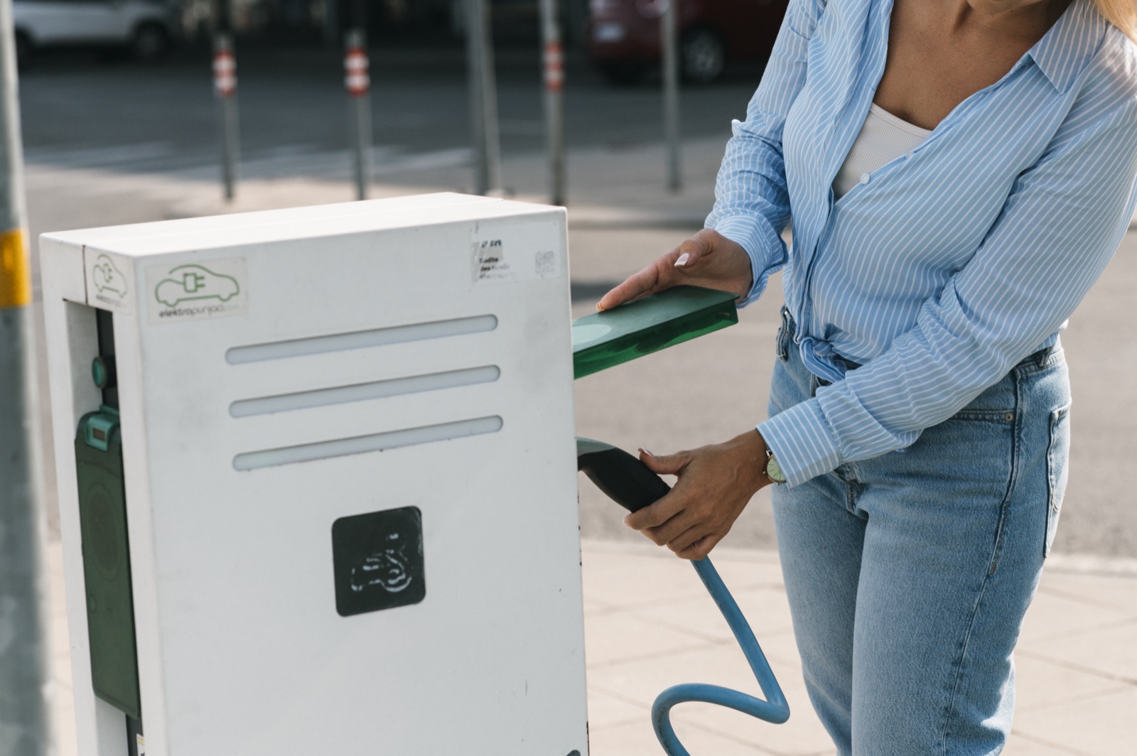 Persona conectando el cable de recarga a un poste de carga para coches eléctricos