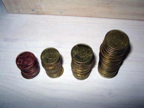 Cuatro torres de monedas de euro de altura creciente sobre una mesa de madera clara