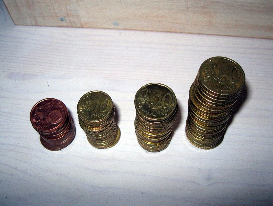 Cuatro torres de monedas de euro de altura creciente sobre una mesa de madera clara