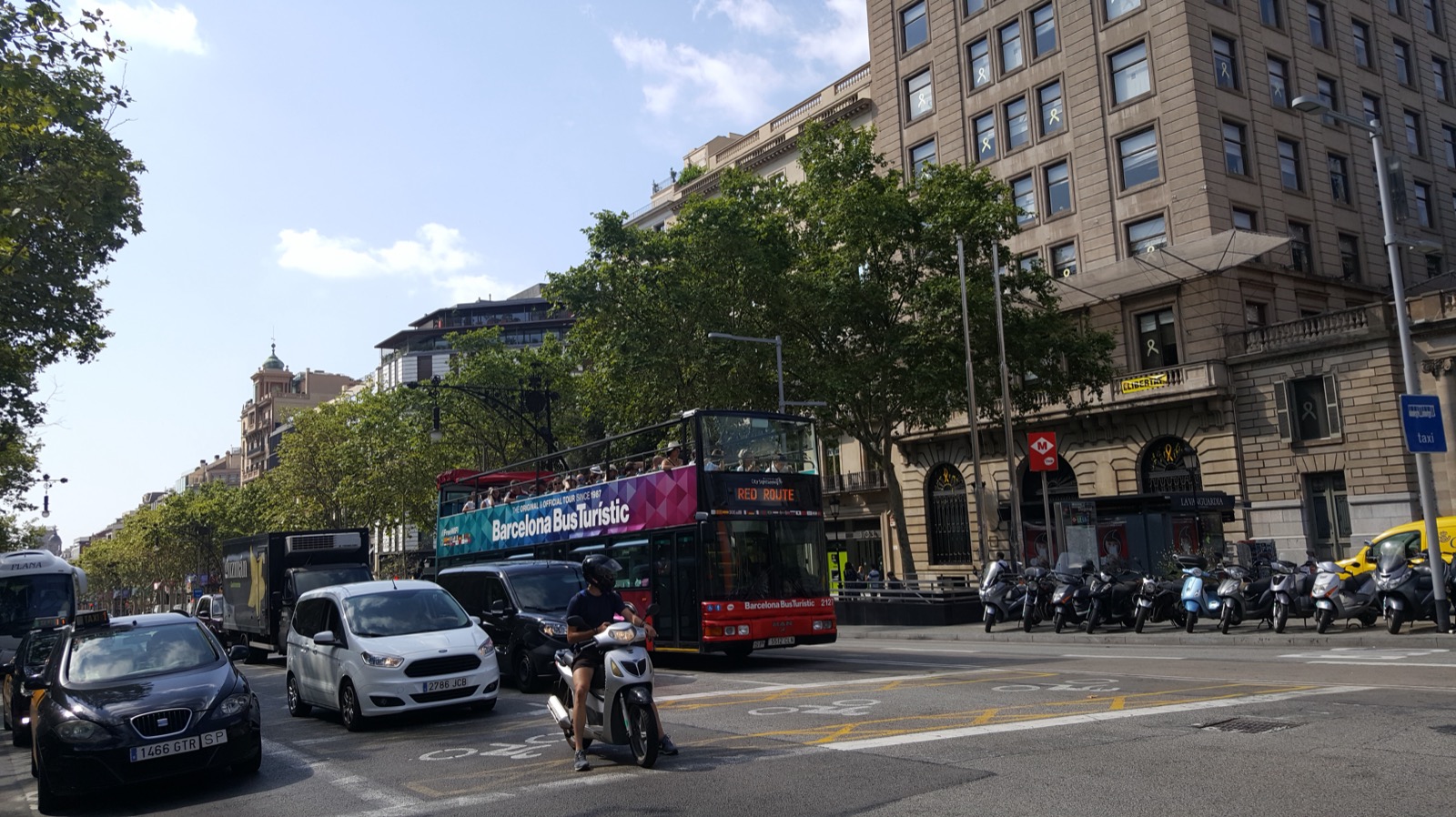 Tráfico denso en una avenida de una ciudad española, con autobús, coches y motos