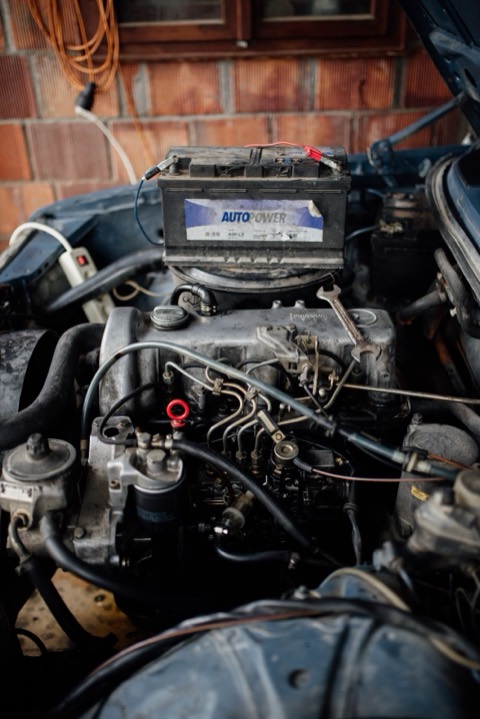 Vano motor abierto de un coche en reparación, con la batería apoyada encima y llaves fijas sobre el motor