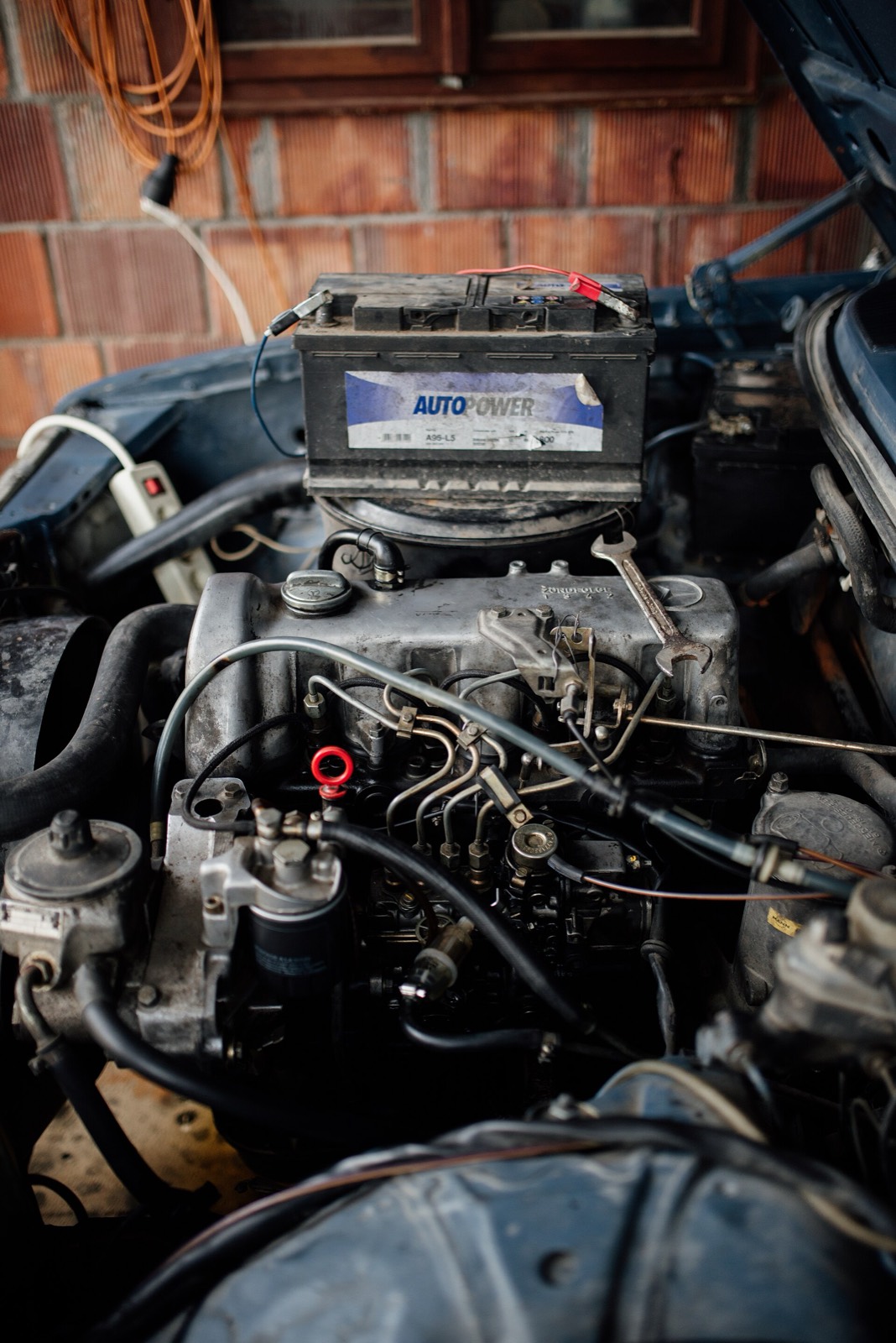Vano motor abierto de un coche en reparación, con la batería apoyada encima y llaves fijas sobre el motor
