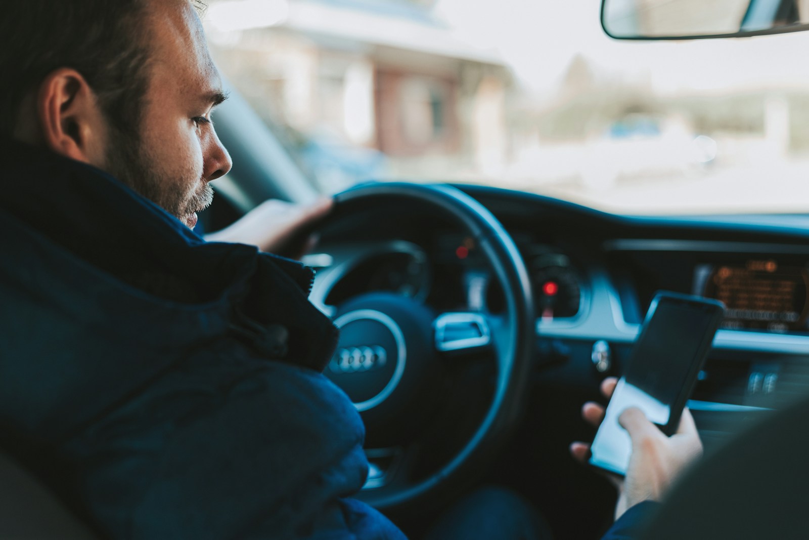 Conductor al volante mirando el teléfono móvil que sostiene en la mano